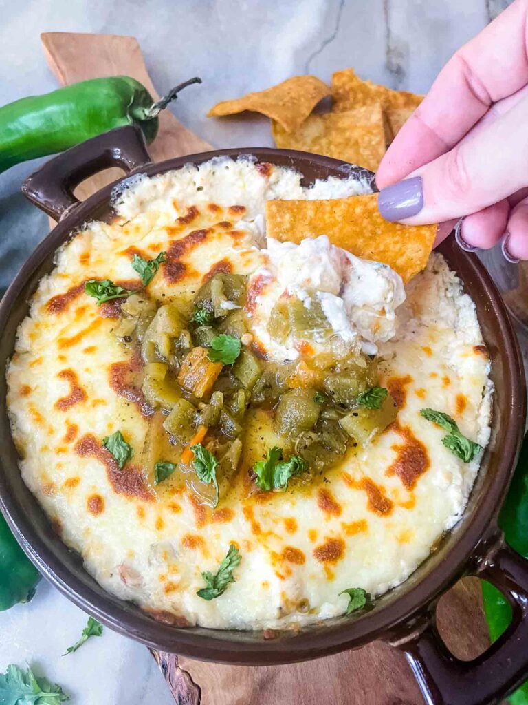 A hand dunking a chip into Hatch Green Chile Cheese Dip