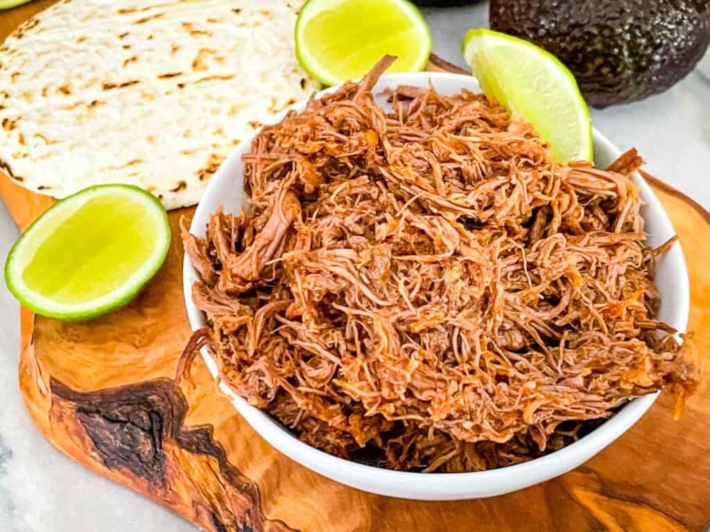 Instant Pot Shredded Beef Barbacoa in a small bowl on a cutting board with limes