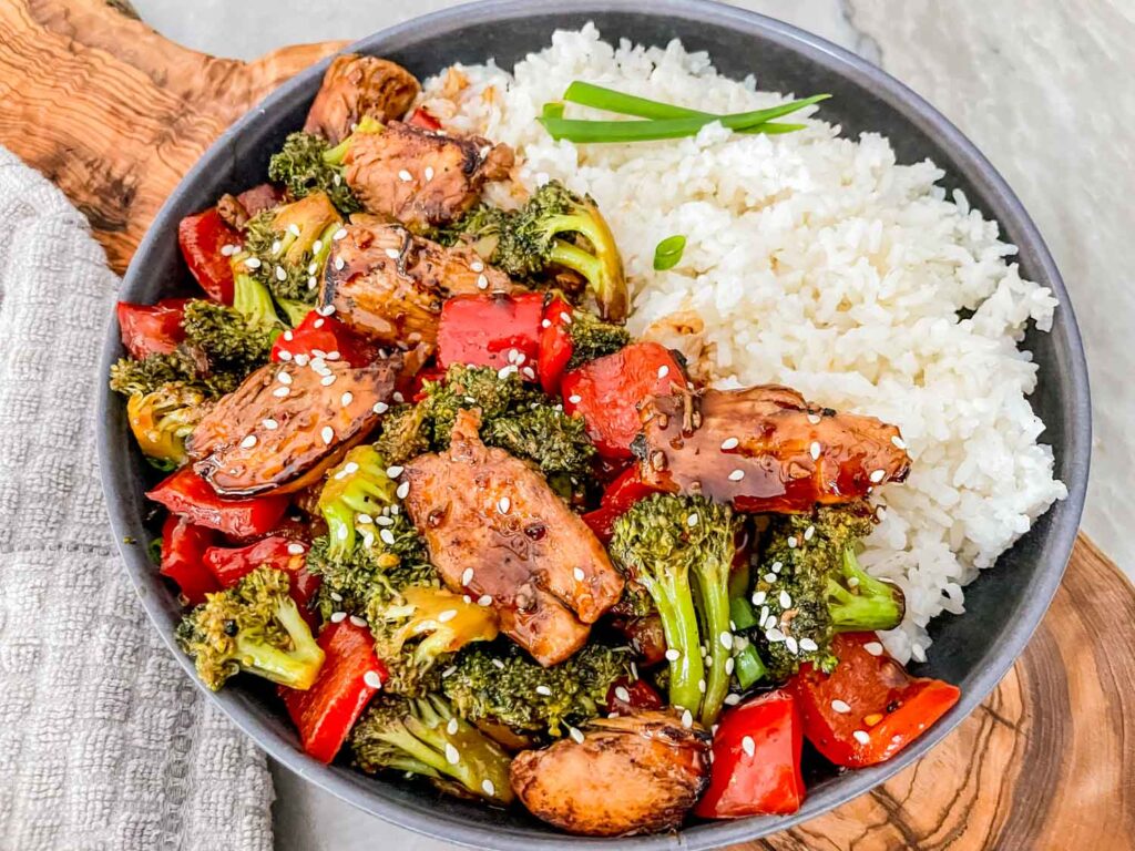 Teriyaki Chicken Stir Fry in a gray bowl with white rice on one side. Sitting on a piece of wood on a counter