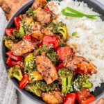 Top view of Teriyaki Chicken Stir Fry in a gray bowl with white rice. Sitting on a wood board on a counter