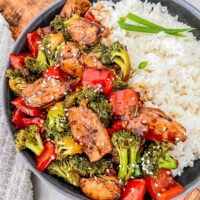 Top view of Teriyaki Chicken Stir Fry in a gray bowl with white rice. Sitting on a wood board on a counter