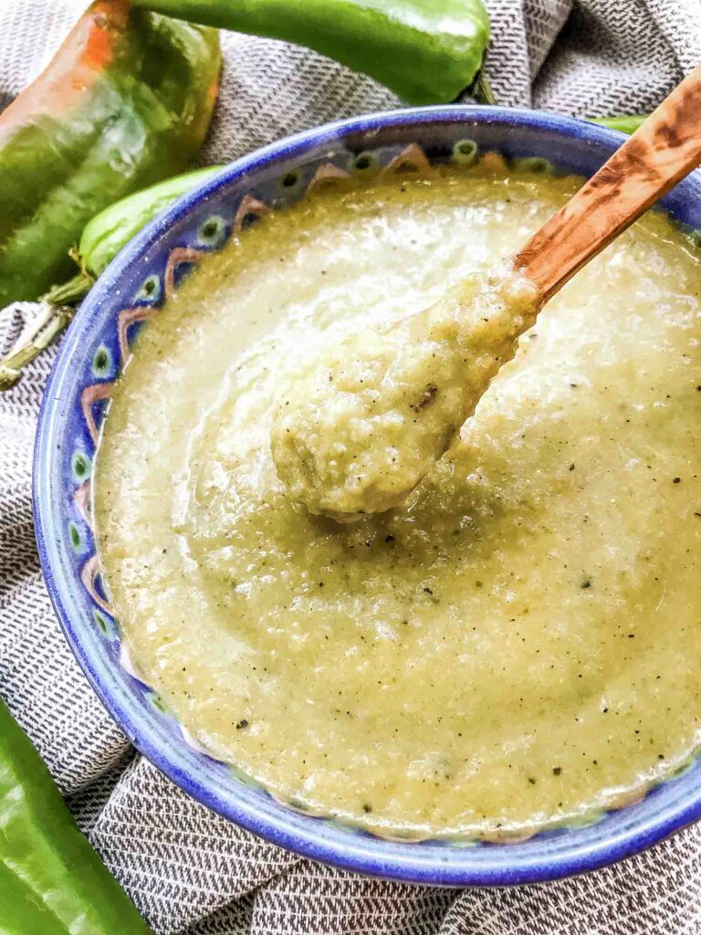A small spoon scooping Hatch Chile Green Sauce for Enchiladas out of a bowl