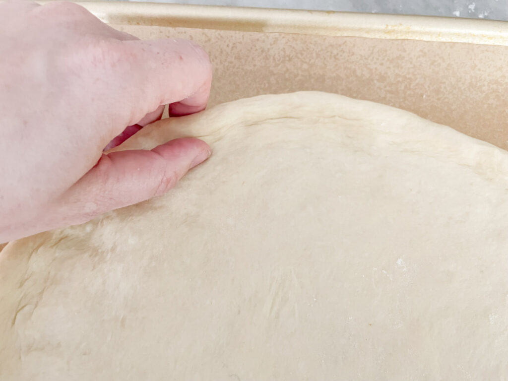 A hand pinching the edge of the rolled out dough to make the crust