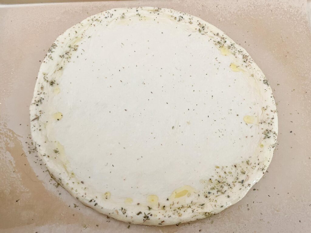 The raw pizza dough rolled out with a seasoned crust edge