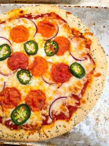 An entire 30 Minute Homemade Pizza topped with peppers, pepperoni, and onion sitting on a baking sheet