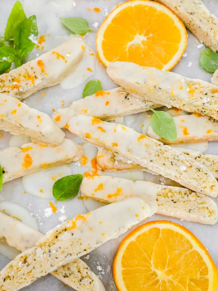 A pile of Basil Orange Biscotti on a counter with basil and orange slices around them