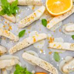 Basil Orange Biscotti scattered on a counter surrounded by fresh basil and orange slices