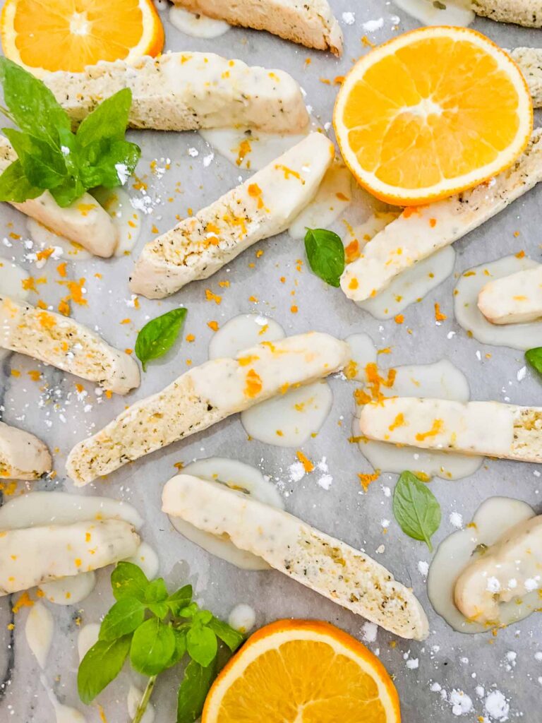 Basil Orange Biscotti scattered on a counter surrounded by fresh basil and orange slices