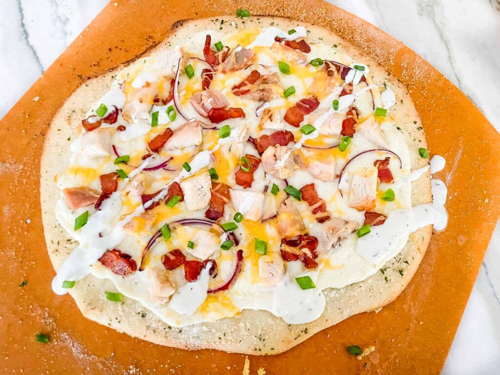 A full Chicken Bacon Ranch Pizza on a pizza peel before being cut