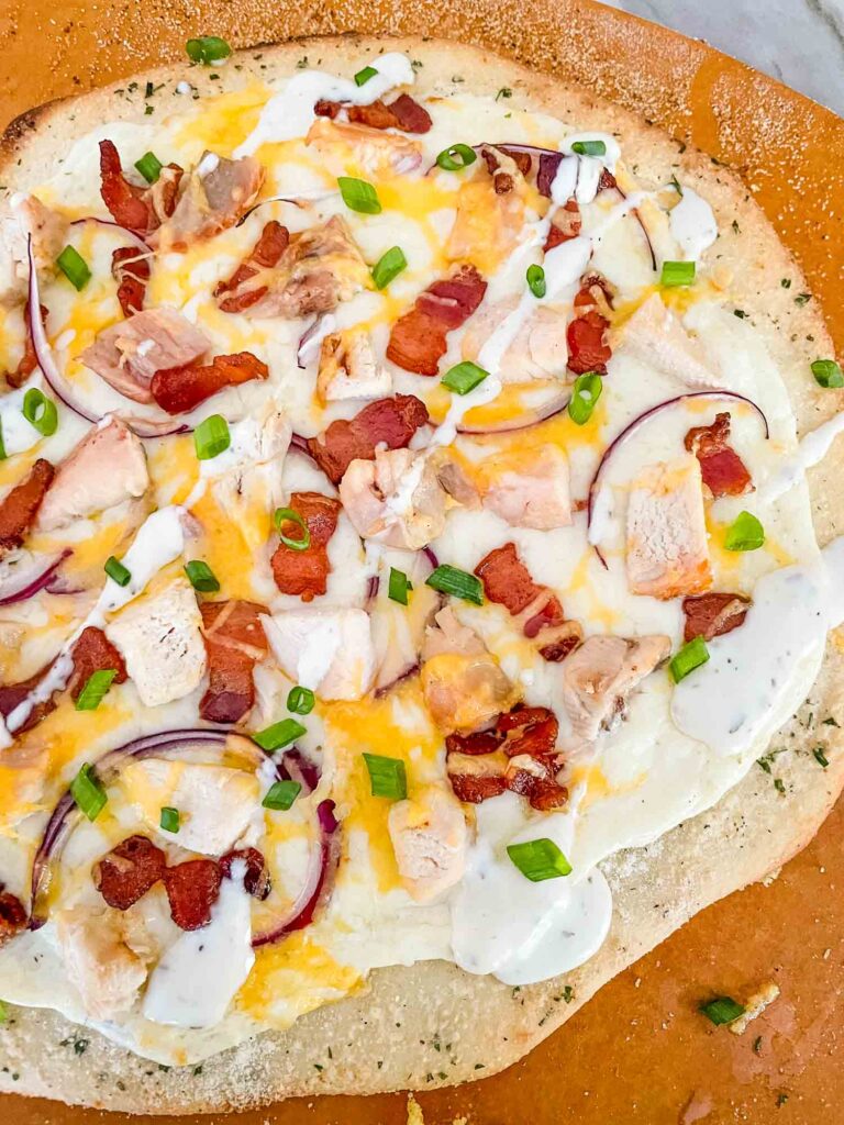 Top view of a Chicken Bacon Ranch Pizza fresh out of the oven on top of a pizza peel