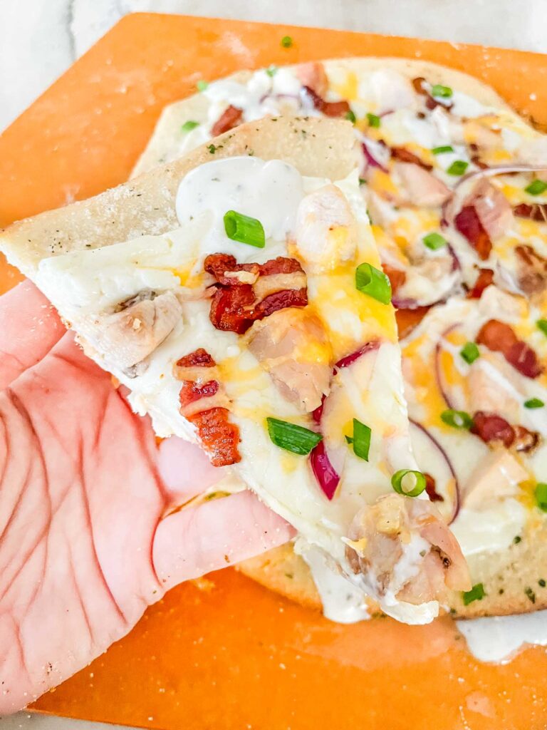 A hand holding a slice of Chicken Bacon Ranch Pizza over the whole pizza