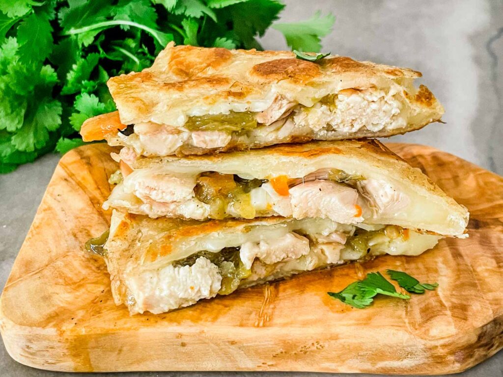 Three Hatch Green Chile Chicken Quesadilla pieces stacked on top of each other on a wood board