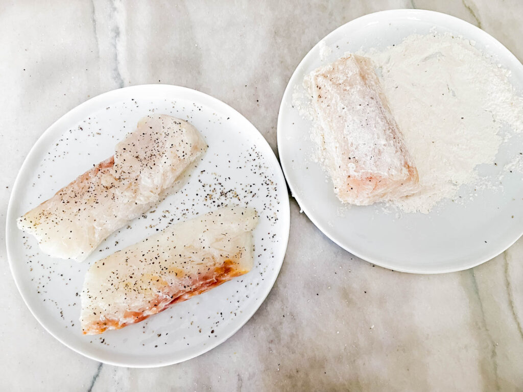 Cod piece being coated in flour on plates, sitting on a counter