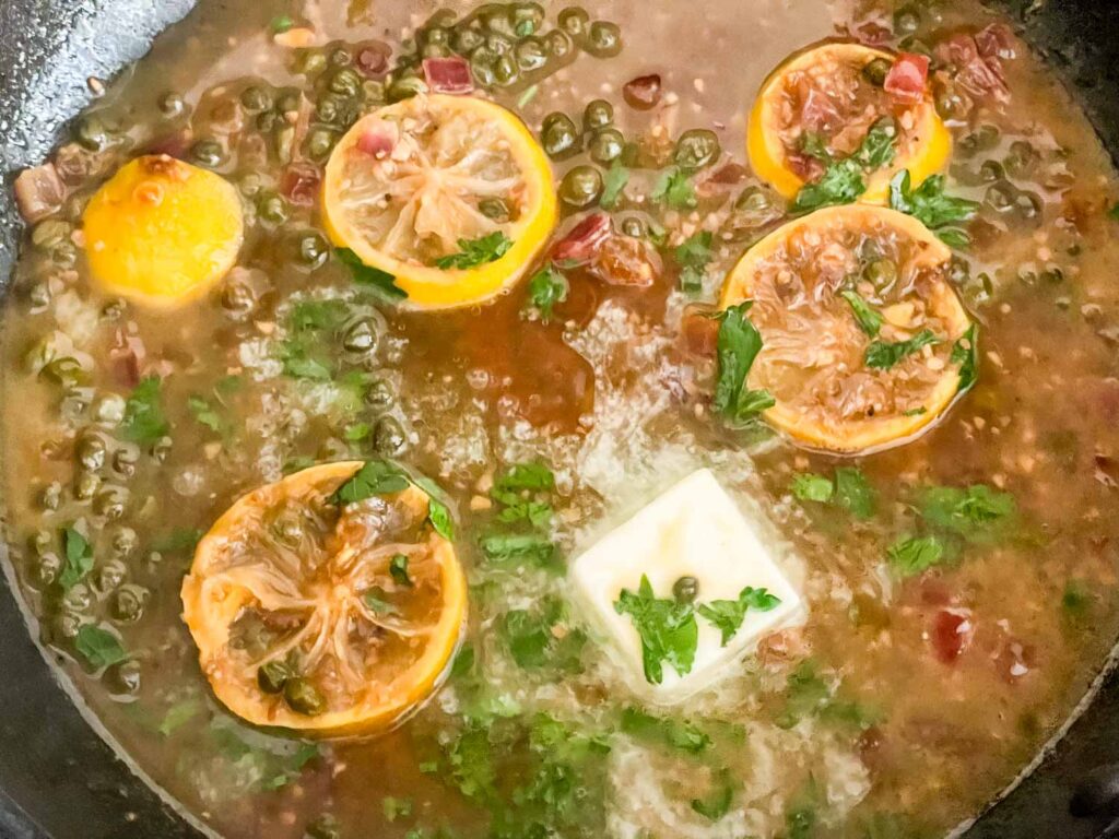 The sauce simmering wit butter, parsley, capers, and lemon slices