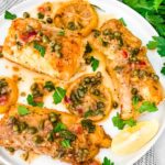 A white plate with pieces of Cod Piccata on it with parsley