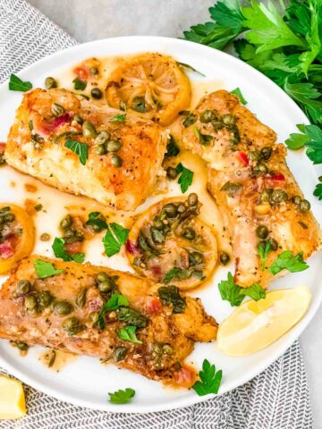 A white plate with pieces of Cod Piccata on it with parsley