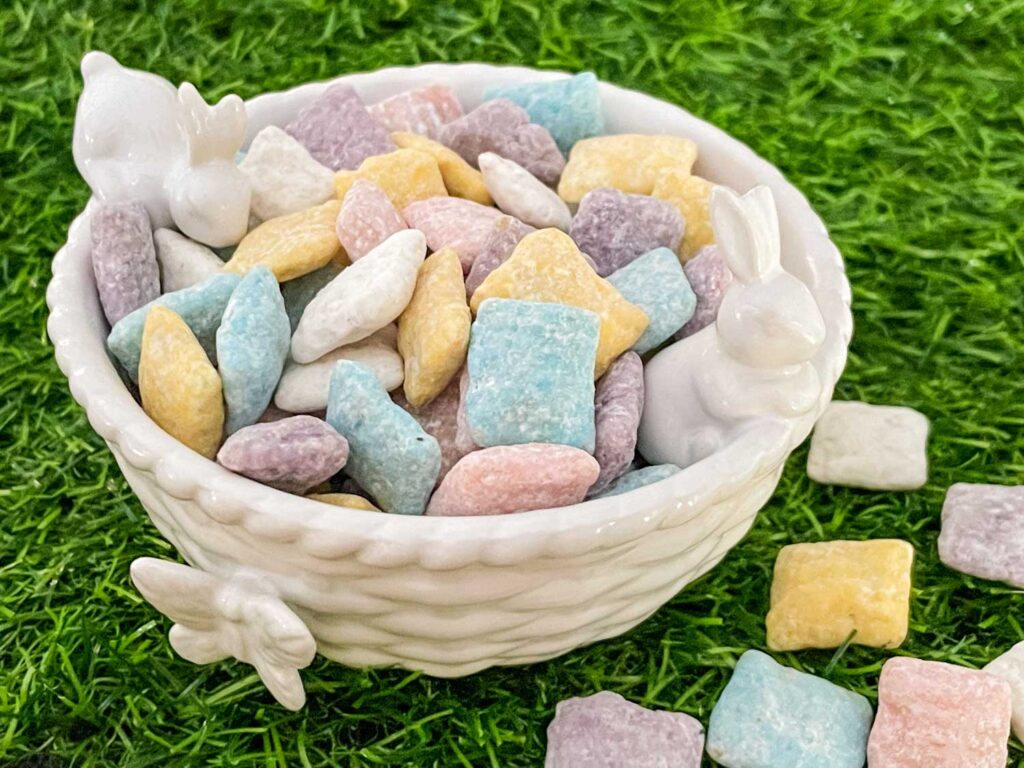 Two bunnies on a white bowl with Easter Puppy Chow inside sitting on green grass