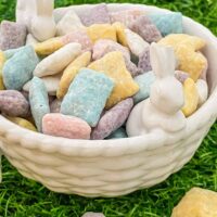 A white ceramic bowl with small bunnies full of the Easter Puppy Chow sitting on green grass