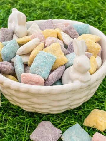 A white ceramic bowl with small bunnies full of the Easter Puppy Chow sitting on green grass