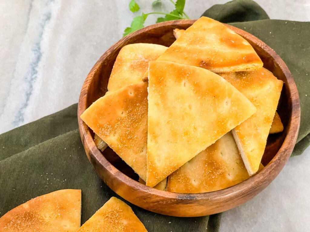 A brown wood bowl full of large Air Fryer Pita Chips sitting on a green napkin