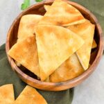 Air Fryer Pita Chips piled up in a small wood bowl sitting on a green napkin on a counter