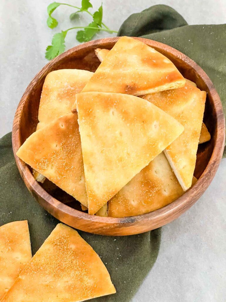 Air Fryer Pita Chips piled up in a small wood bowl sitting on a green napkin on a counter