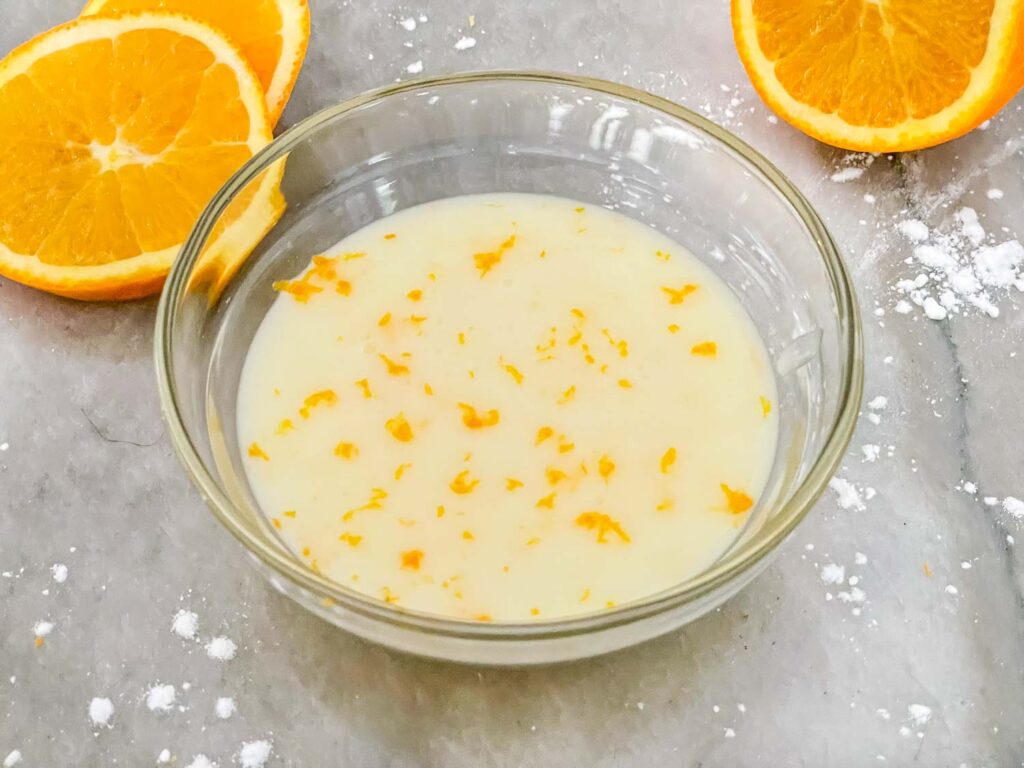 Orange Glaze in a clear bowl on a counter with oranges around it