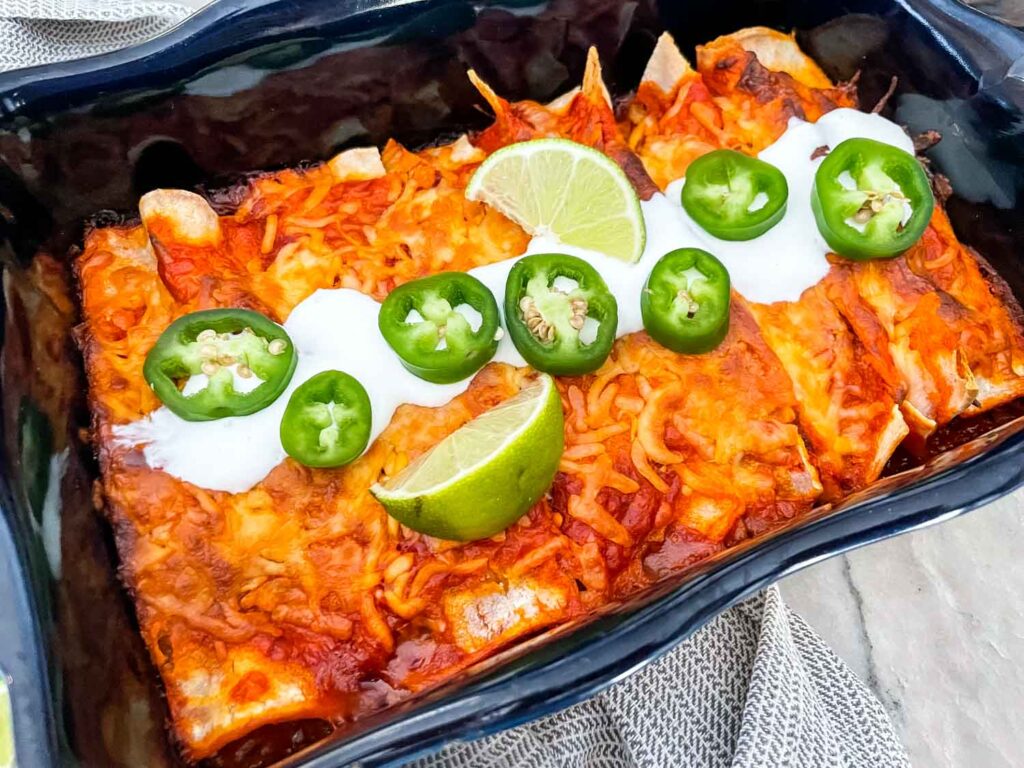 Top view of a full dish of Shredded Beef Enchiladas with sour cream, jalapeno, and lime on top