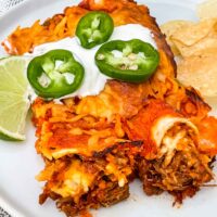 Two Shredded Beef Enchiladas on a plate with sour cream and jalapenos on top