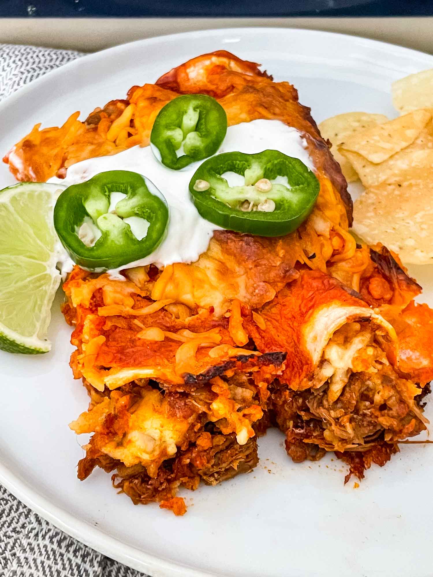 Two Shredded Beef Enchiladas on a plate with sour cream and jalapenos on top
