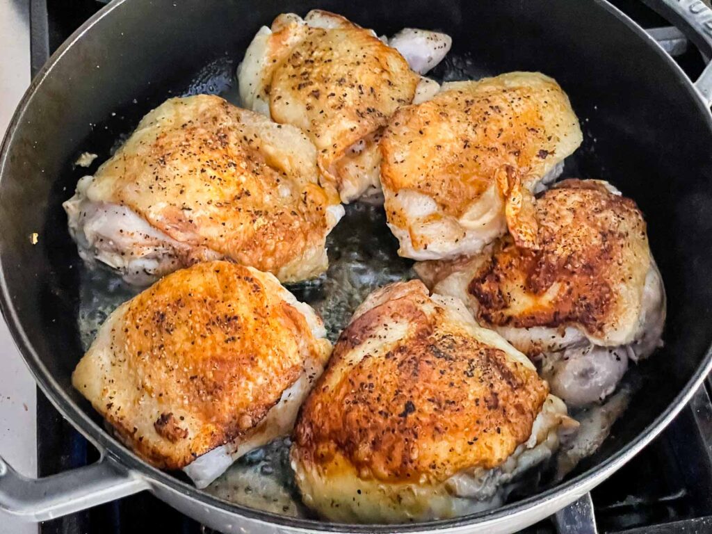 The chicken being browned inside the braiser on the stove