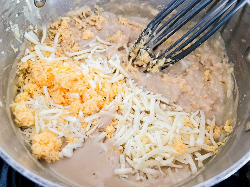 A whisk mixing the cheese into the sauce mixture in a pot