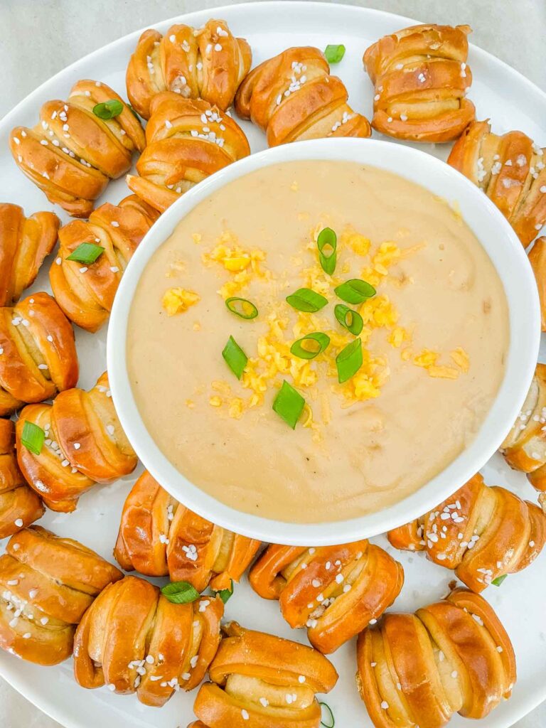 Top view of Beer Cheese Dip in a small bowl sitting on a plate of soft pretzel bites