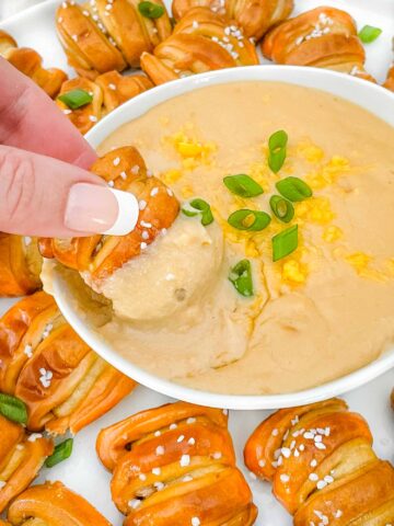 A hand dunking a soft pretzel piece into a bowl of Beer Cheese Dip