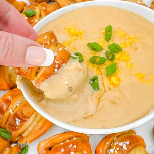 A hand dunking a soft pretzel piece into a bowl of Beer Cheese Dip
