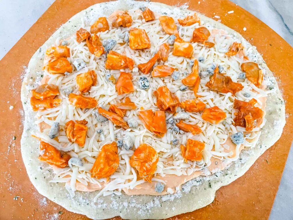 The pizza crust being topped with the sauce, cheeses, and chicken before cooking