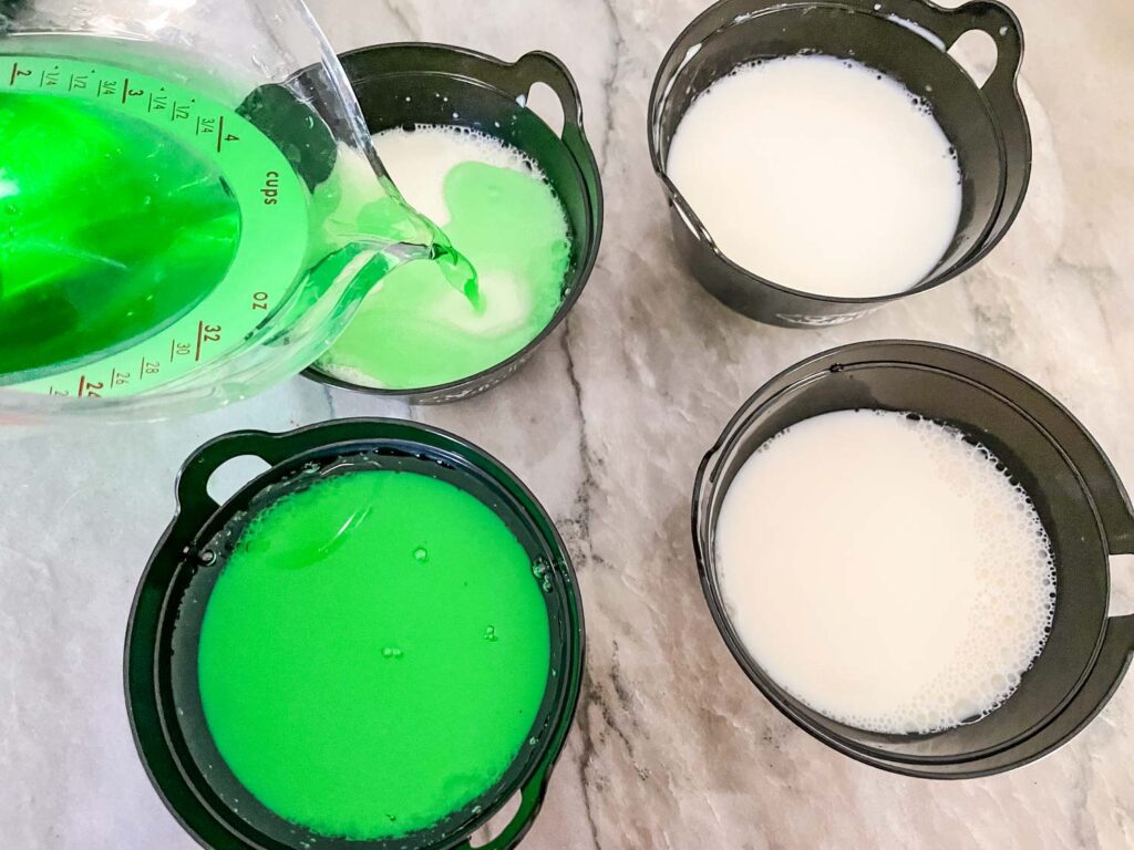 Pouring the green jello on top of the white inside of plastic cauldrons