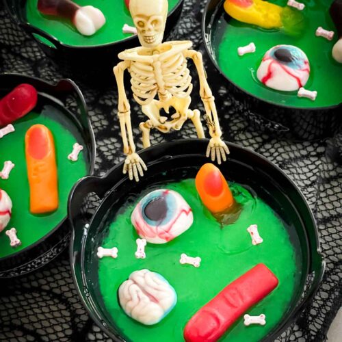 A skeleton standing at a green Halloween Jello Cauldron with gummy body pieces in it