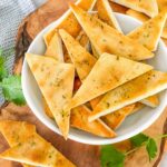 Small Homemade Baked Pita Chips triangles piled in a small white bowl on a wood board sitting on a counter