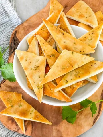 Small Homemade Baked Pita Chips triangles piled in a small white bowl on a wood board sitting on a counter