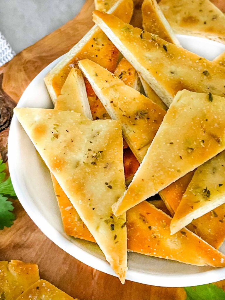 Closer view of Homemade Baked Pita Chips in a small white bowl sitting on a wood board