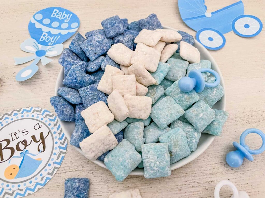 Dark blue white, and light blue It's a Boy Puppy Chow separated by color on a small plate on a table with decorations around it