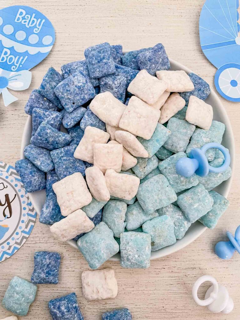 Dark blue, white, and light blue It's a Boy Puppy Chow separated by color on a small plate sitting on a white table