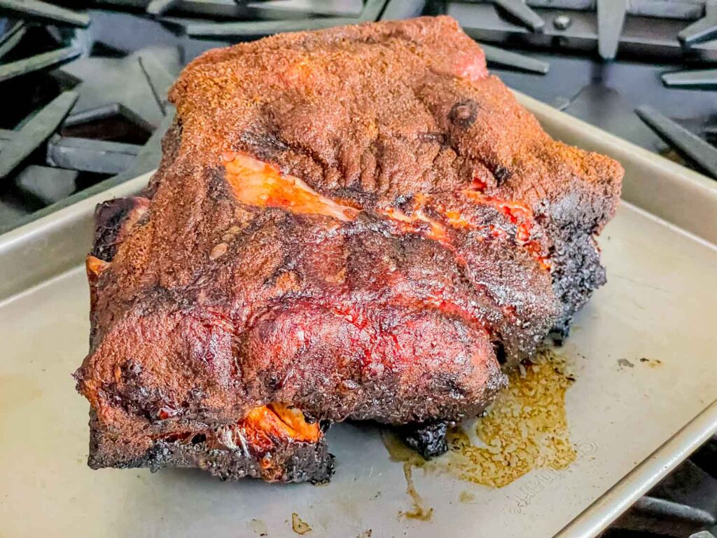 A whole Smoked Pork Butt sitting on a baking sheet on an oven