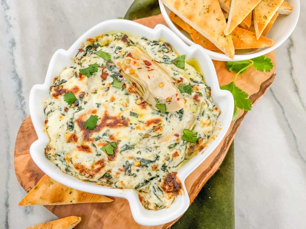 Easy Spinach Artichoke Dip in an artichoke shaped dish on a wood board on a counter