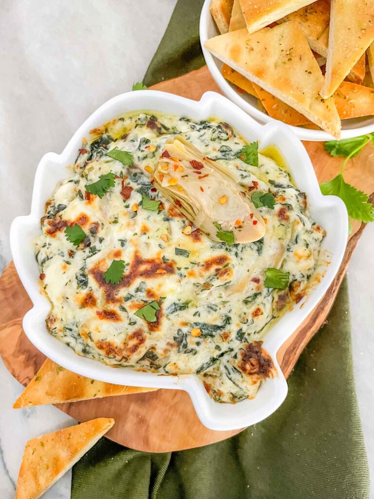 Top view of Easy Spinach Artichoke Dip in an artichoke shaped dish on a wood board