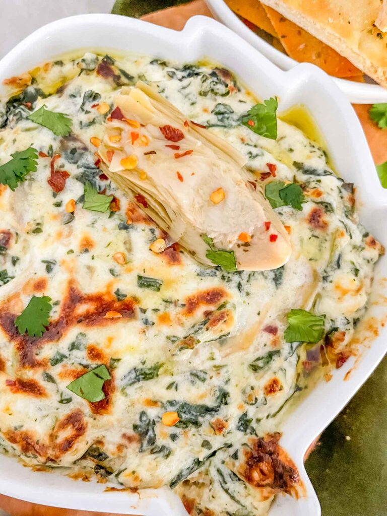 Close view of the dip in an artichoke shaped dish with an artichoke heart on top