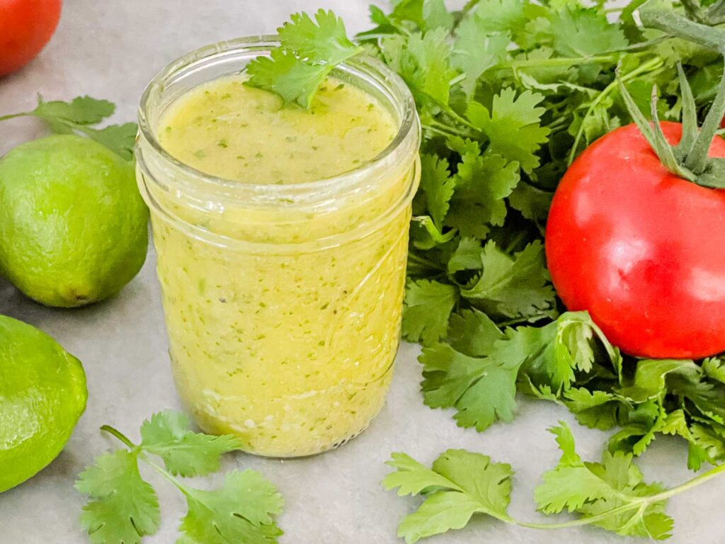 Cilantro Lime Vinaigrette Salad Dressing in a jar on a counter surrounded by fresh cilantro