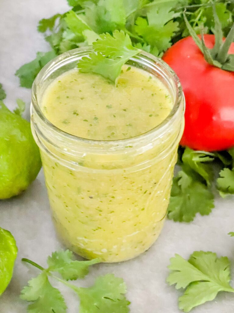 A clear jar full of Cilantro Lime Vinaigrette Salad Dressing on a counter with fresh cilantro around it