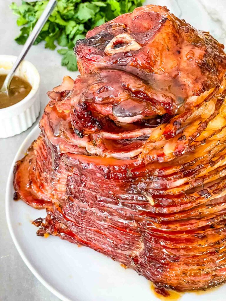 A whole Honey Mustard Glazed Spiral Ham on a white plate on a counter